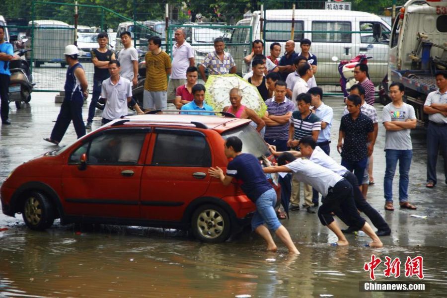 6月13日早上6时许，广西柳州市下起倾盆大雨，致使该市柳江区拉堡镇乐都大道涵洞积水约2米，多辆停放在此的车辆被水泡。该涵洞还未启用，附近不少居民将此处当停车场，而入口处被绿色的铁丝网围住，悬挂着“施工重地，闲人免进”，“施工通道，禁止停车”等字样的警示牌。图为人们将车辆推出淹水地带。 朱柳融 摄